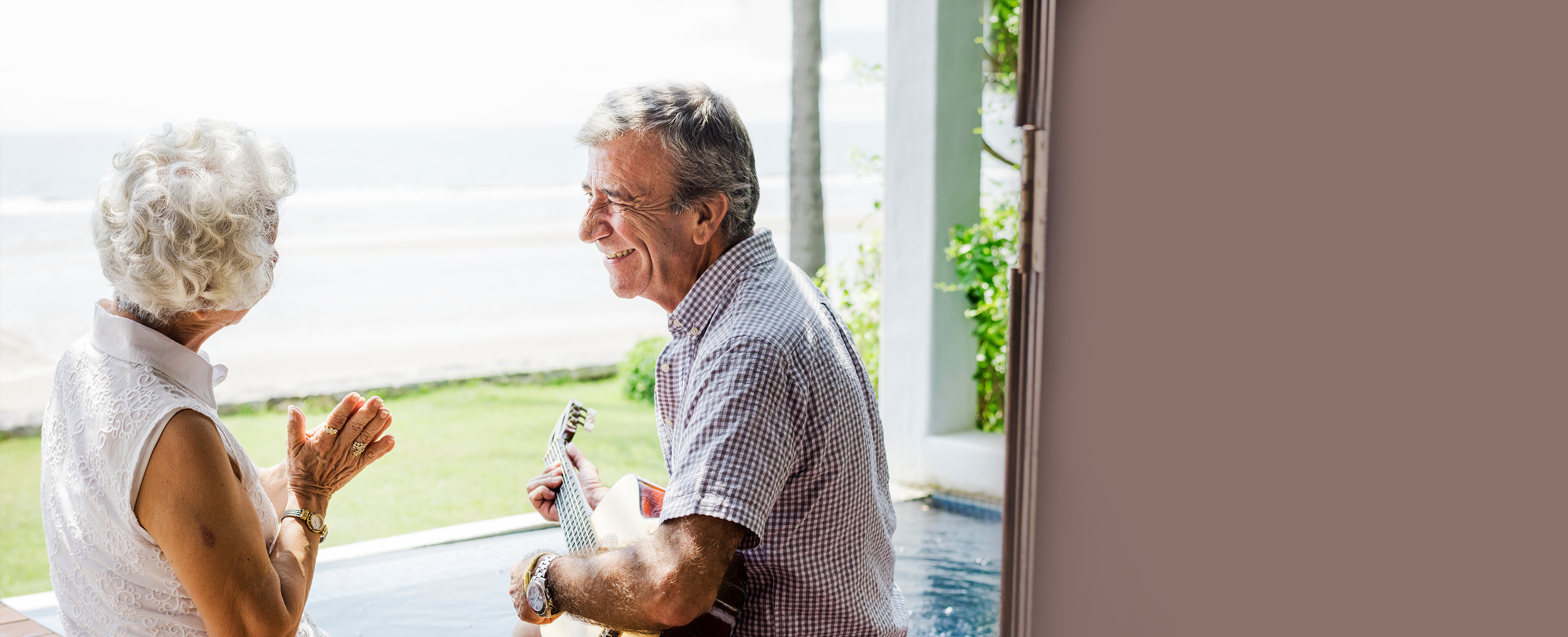Elderly man playing guitar for a delighted older woman.